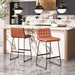 Two brown bar stools in a modern kitchen with marble countertops and pendant lights.