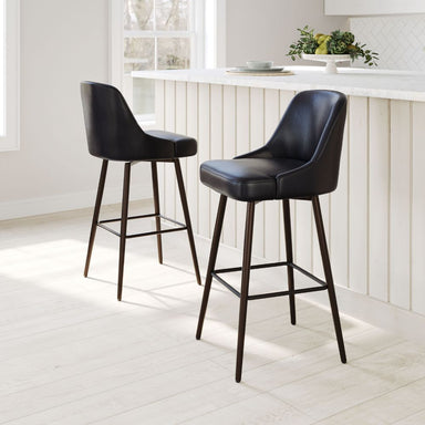Two black bar stools in a modern kitchen setting with white countertops and light wood flooring.
