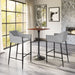 Modern bar height table with gray chairs in a bright room with large windows.