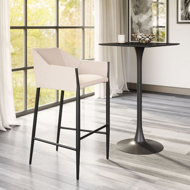 Modern bar stool with white cushioned seat next to a black bar table in a bright room with large windows.