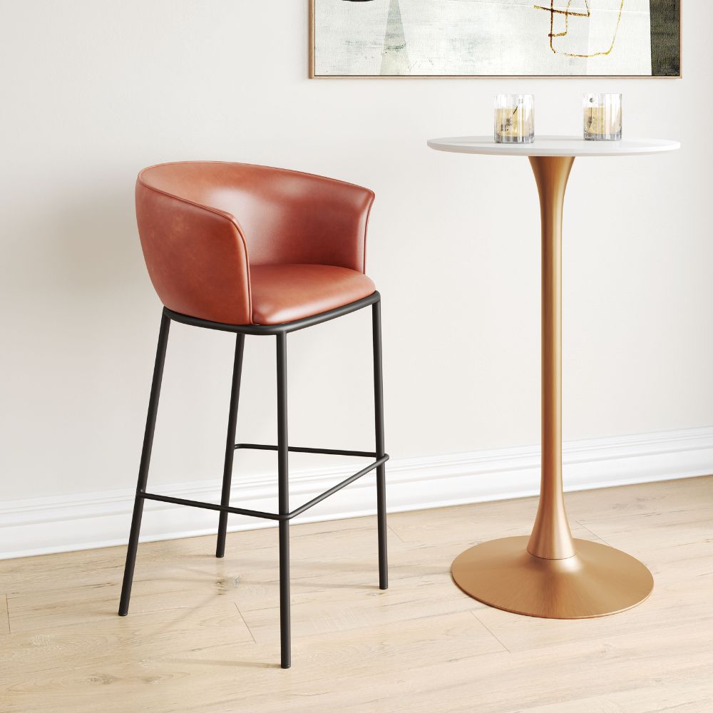 Brown leather bar stool next to a gold pedestal table with candles on a light wood floor.