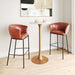Two brown leather bar stools in front of a small round table with a gold base.
