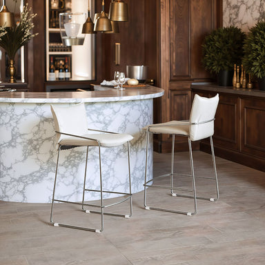 Two white bar stools in front of a marble island in a kitchen setting.