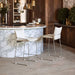 Two white bar stools in front of a marble island in a kitchen setting.