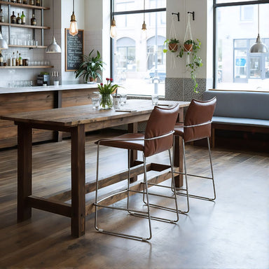 Modern kitchen with wooden dining table and brown bar stools, large windows, and decorative plants.