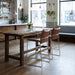 Modern kitchen with wooden dining table and brown bar stools, large windows, and decorative plants.