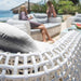 White wicker chair with blurred background of people sitting on a couch by a body of water.