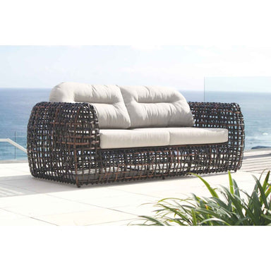 Wicker outdoor sofa with white cushions on a patio with ocean view