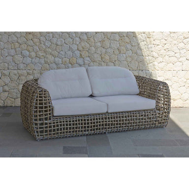 Wicker outdoor sofa with light gray cushions against a stone wall.