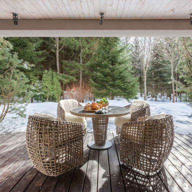 Wicker chairs and table on a wooden deck with snow-covered ground and trees in the background