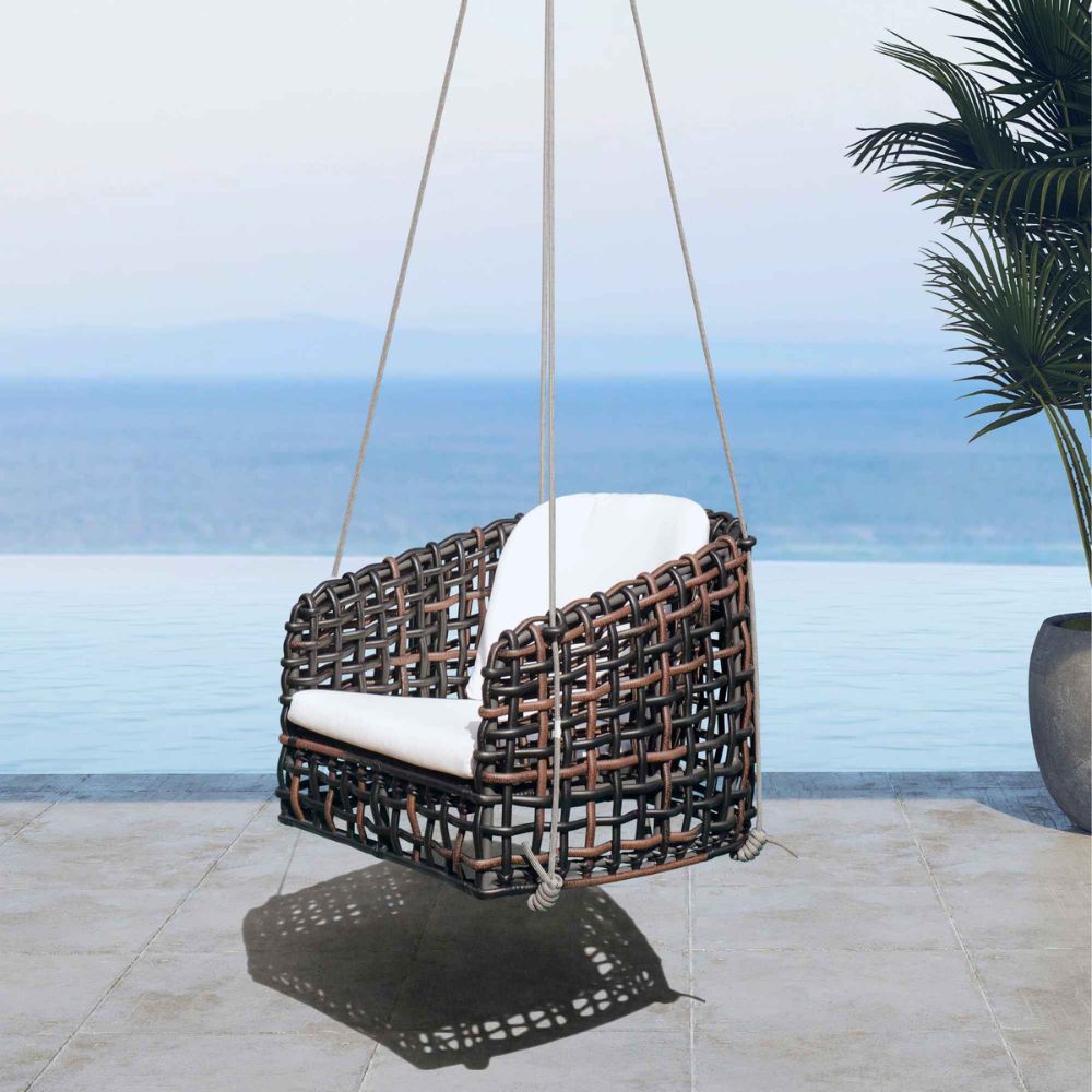 Wicker swing chair with white cushion hanging on a patio with ocean view