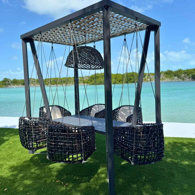 Outdoor swing set with black ropes and chairs against a scenic water background