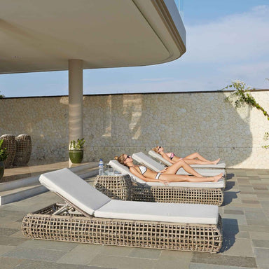 Two women relaxing on wicker lounge chairs by a poolside.