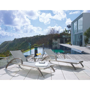 Two lounge chairs on a patio with a pool and scenic view in the background