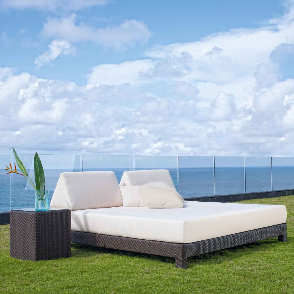 Outdoor patio set with white cushions on a grassy area overlooking the ocean.