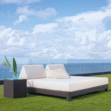 Outdoor patio set with white cushions on a grassy area overlooking the ocean.