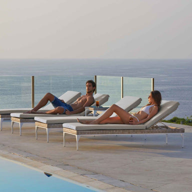 Two people relaxing on lounge chairs by a pool with ocean view