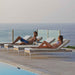 Two people relaxing on lounge chairs by a pool with ocean view