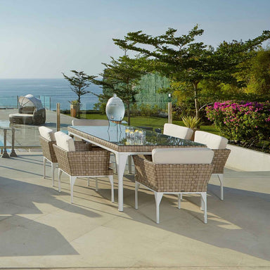 Outdoor dining set with a glass table and wicker chairs on a patio with ocean view.