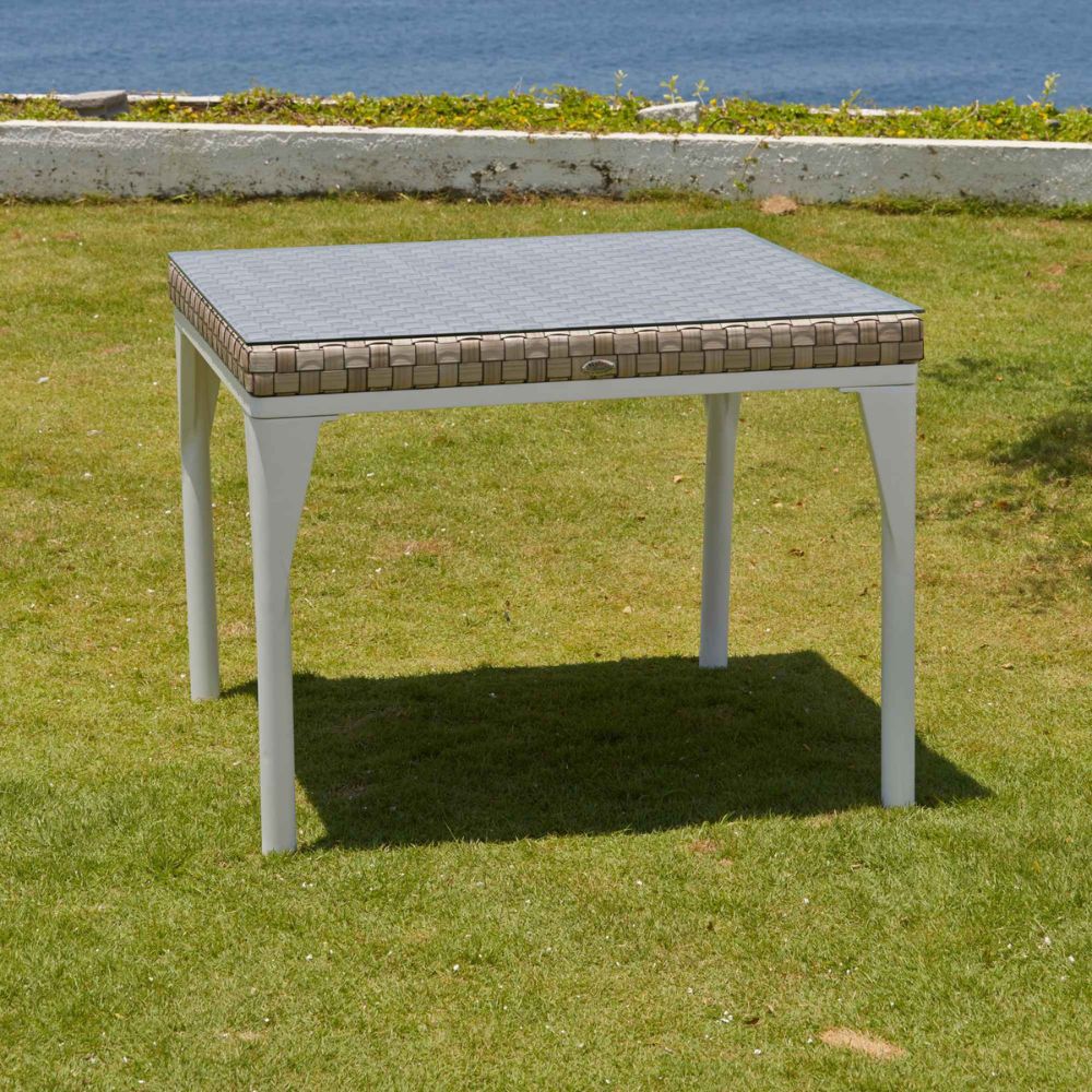 Square outdoor table with a textured top on grass with ocean view