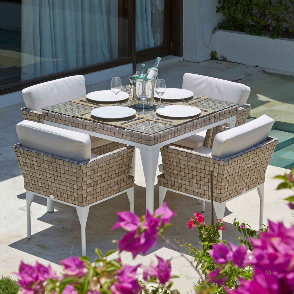 Outdoor patio set with table and chairs near a pool, surrounded by flowers.