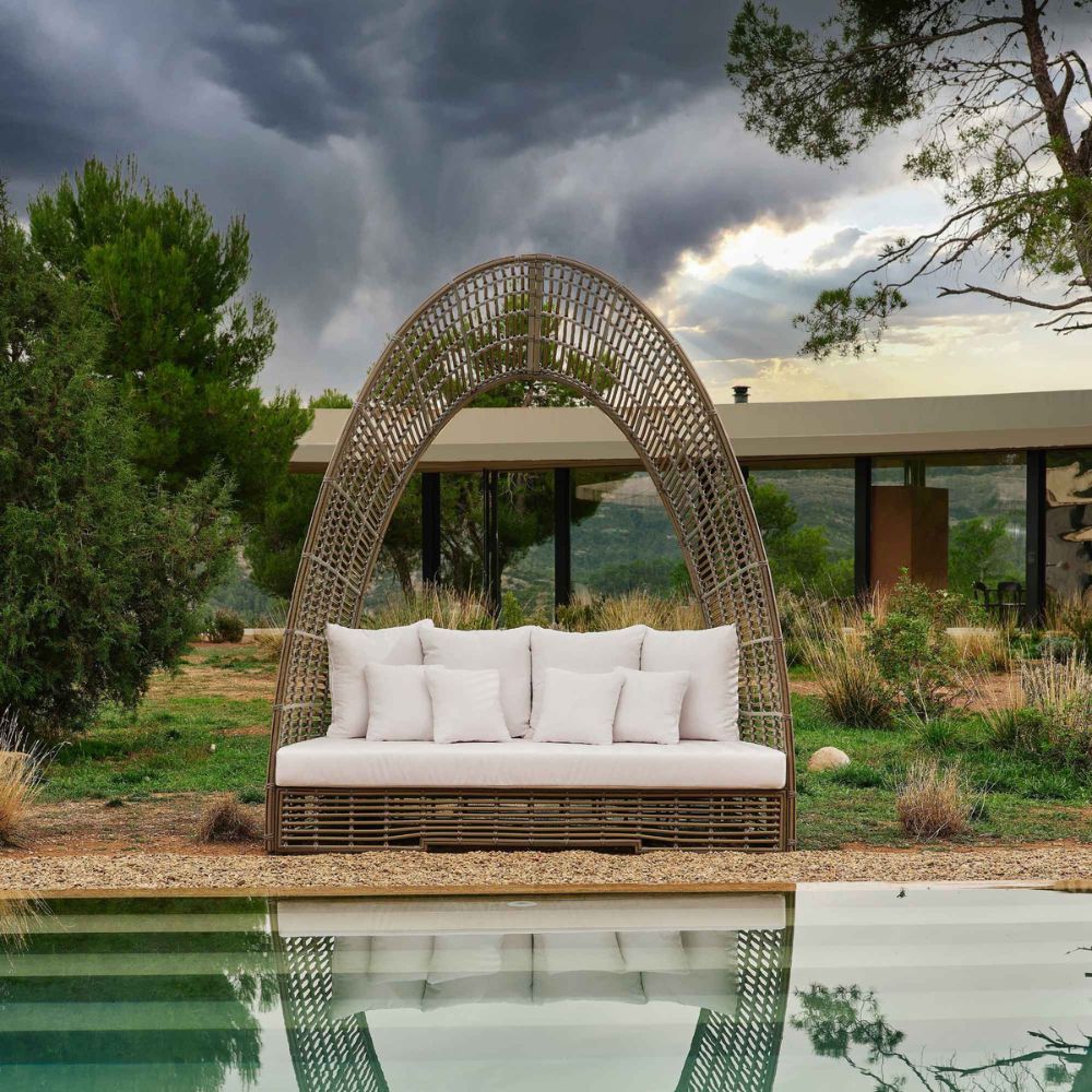 Wicker chair with white cushions by a pool under a cloudy sky
