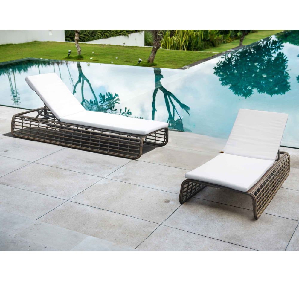 Two lounge chairs with white cushions on a patio by a pool.