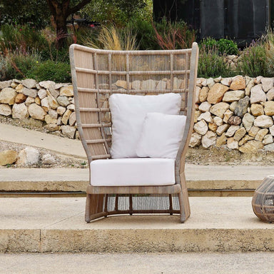 Wicker chair with white cushions on a stone patio with a stone wall and garden in the background