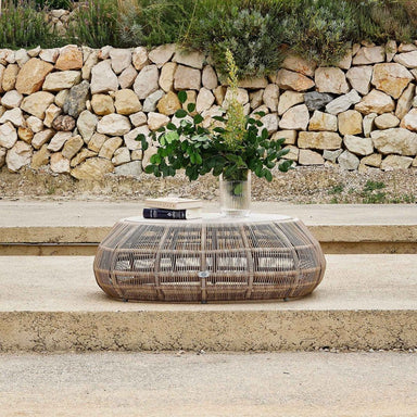 Wicker table with a vase of flowers on stone steps, stone wall in the background
