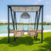 Outdoor swing set with wicker chairs and table under a canopy by a body of water.