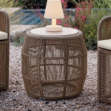 Wicker side table with a lamp on it, surrounded by outdoor furniture and plants.