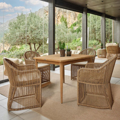 Outdoor patio with wooden table and wicker chairs, surrounded by greenery.