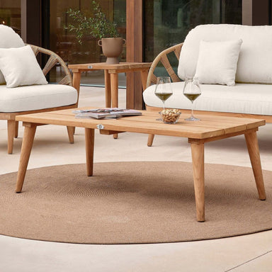 Outdoor patio setting with wooden coffee table, chairs, and a rug.