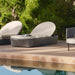 Wicker outdoor lounge chair with cushion on a wooden deck by a pool
