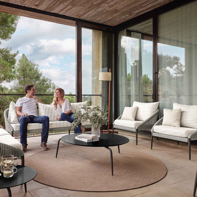 Two people sitting on a modern outdoor patio with large glass windows and chairs.