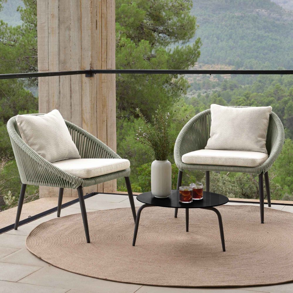 Two green chairs with white cushions on a patio with a scenic view of trees and mountains.