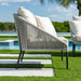 Outdoor chair with white cushions on a patio with a pool and greenery in the background