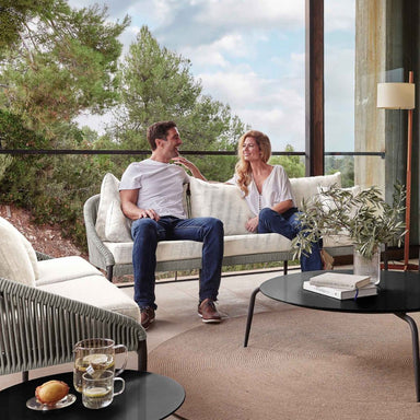 Two people sitting on a sofa in a modern living room with a view of trees.