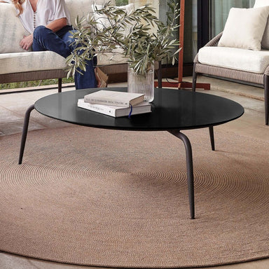 Round black coffee table with books and a plant in a living room setting
