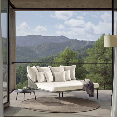Modern outdoor sofa with scenic mountain view through large glass doors.