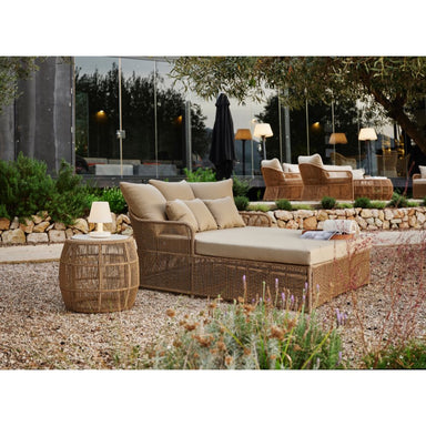 Outdoor patio set with wicker furniture and beige cushions in a garden setting.