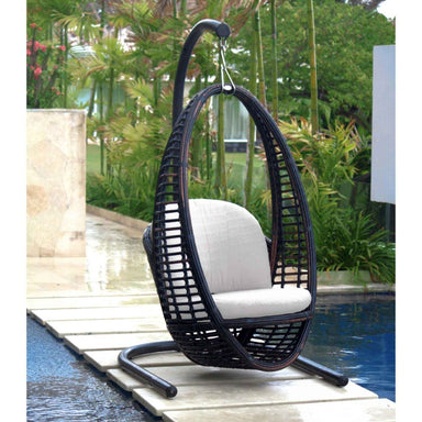 Black wicker hanging chair with white cushion on a wooden platform by a pool