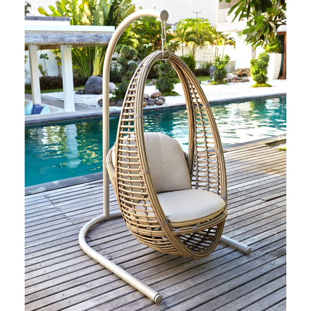 Wicker egg chair with beige cushions on a wooden deck by a pool