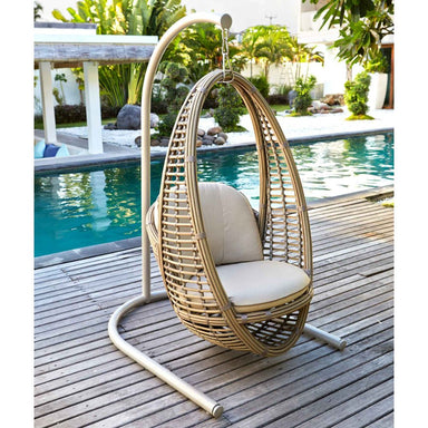 Wicker egg chair with beige cushions on a wooden deck by a pool