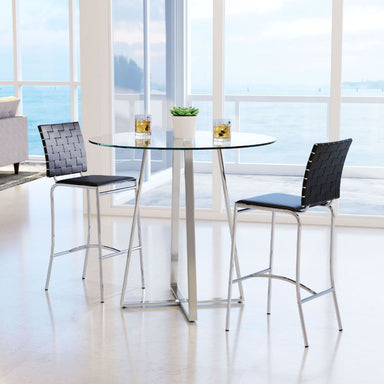 Modern high table with two black chairs in a bright room with large windows.