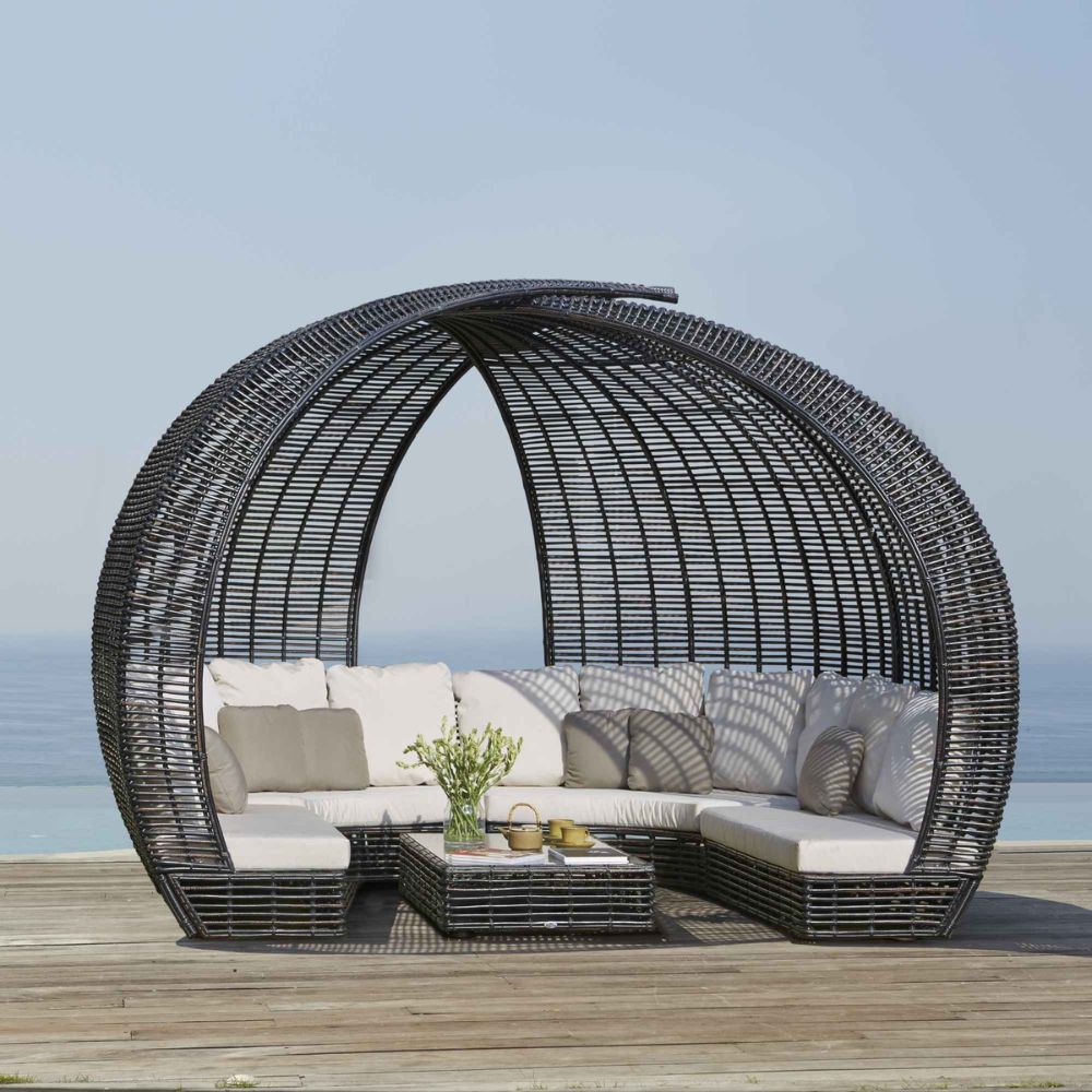 Outdoor patio furniture set with a circular wicker canopy on a wooden deck by the sea.