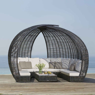 Outdoor patio furniture set with a circular wicker canopy on a wooden deck by the sea.