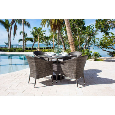 Outdoor patio set with table and chairs by a poolside with palm trees and ocean view.