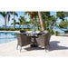 Outdoor patio set with table and chairs by a poolside with palm trees and ocean view.