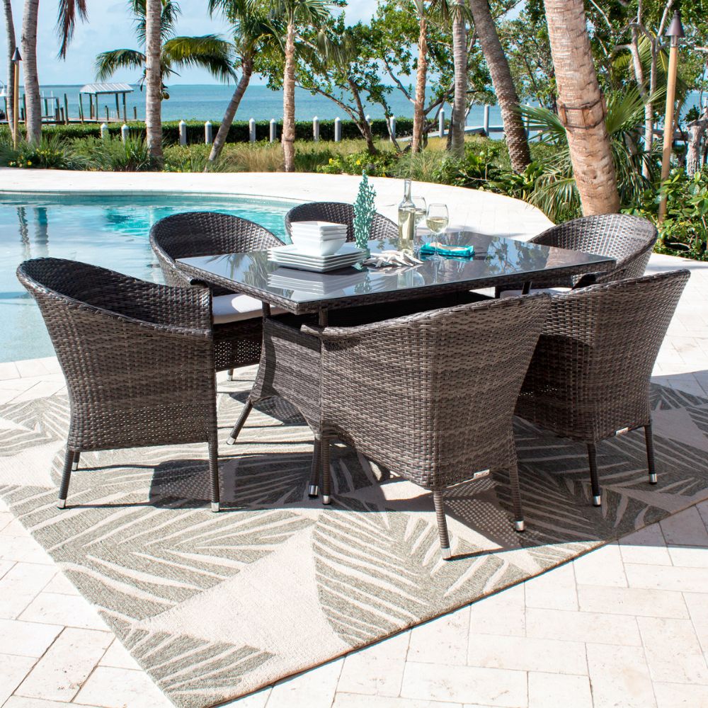 Outdoor dining set with table and chairs on a patio by a pool with palm trees and ocean view.